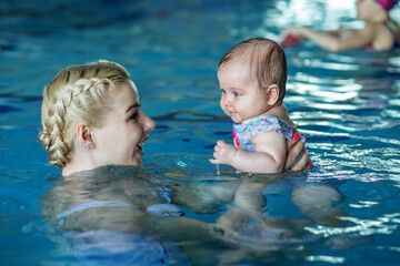 Young beautiful blonde mother with baby in pool. Concept of sport, training and family