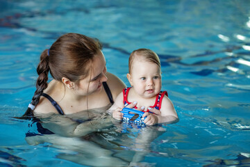 Fototapeta na wymiar Smiling happy mother with baby girl in swimming pool. Sport, training and family concept