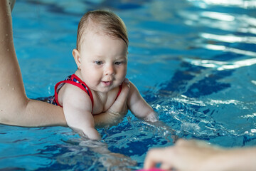 Fototapeta na wymiar Mom supports baby with hands in swimming pool, teaches to swim and dive.