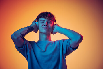 Emotional young red-headed man in headphones listening to music isolated over yellow background in neon. Concept of youth, fashion, emotions, facial expression