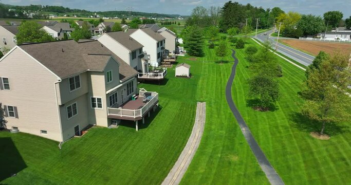Aerial view of backyards of large houses in American neighborhood. Beautiful green grass and trees on spring day.