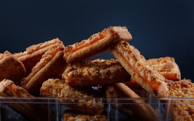 Orange cookies in a plastic container on a dark background .