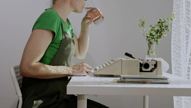 Female playwright drinks water before typing a text early in the morning. Closeup