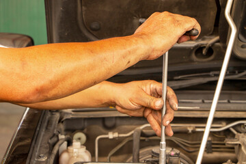 Mechanic's hands holding a wrench working repairing a car engine in a garage