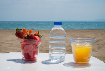  Water plastic bottle and fruits on a plastic cup, and juice on a white table. Beach background