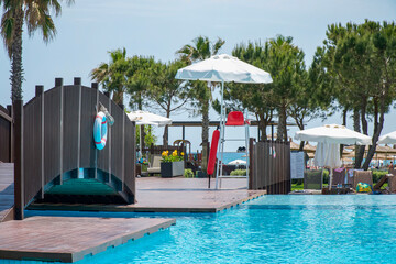 Swimming pool. Empty lifeguard seat with red chair under a white umbrella on a tower by the pool