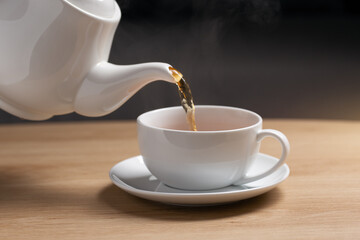 Pour hot tea into a white cup placed on a wooden table