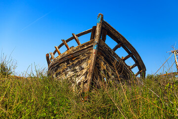 the alone wreck of a dilapidated boat on land covered with grass