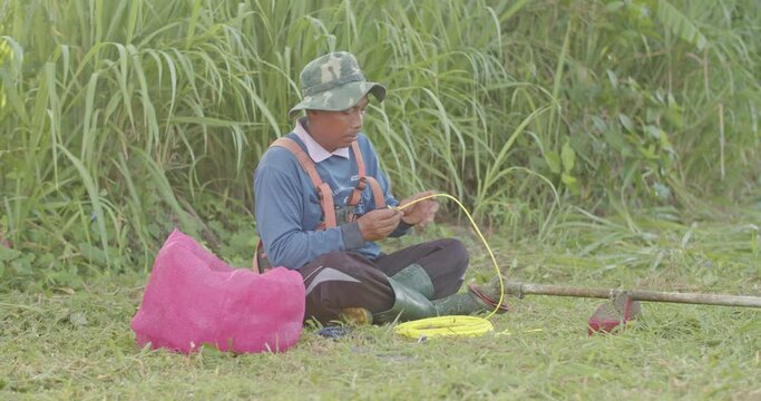 Asian male farmer tanned skin wearing a blue shirt, Change the blade used to cut the grass.