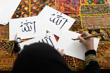 close up muslim girl hands writing Arabic text with bamboo pens and black ink on paper, Arabic...