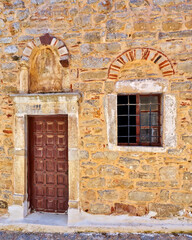 An old stone house front with a brown wooden door and a window. Pyrgi, Chios island, Greece.