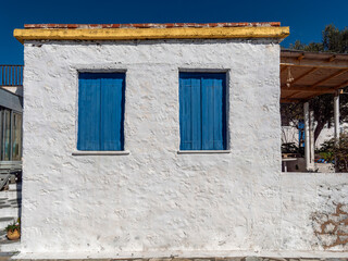 An old house with whitewashed walls and two closed blue shutters windows, Perdika village, Aegina island, Greece.