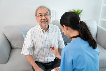 Asian young woman caregiver doctor using stethoscope to checking heartbeat elderly man patient in room during home visit