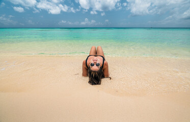 young hispanic woman lying on sand looking back wearing sunglasses - Powered by Adobe