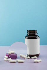 Open bottle for medicines with scattered capsules on a blue background with a blank label.