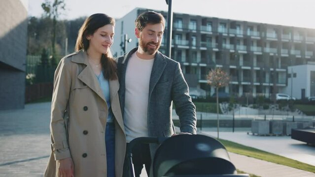 Portrait happy young family walking with a pram near the lake. Husband and wife with baby at sunlight. Parenthood. Slow motion