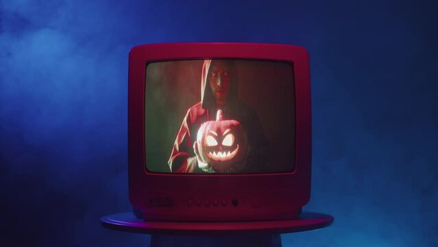 Old tv screen showing Jack-o-lantern close-up. Carved pumpkin on television. Horror film concept, mystery, halloween time. 