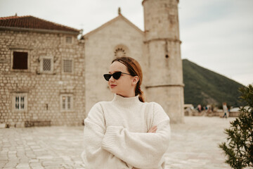 A girl in sunglasses and a white suit walks on the island. Travel, Montenegro. Boka island Church of Our Lady of the Rocks Kotor Bay.