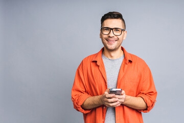 Great news today! Happy smiling young ukrainian man in casual standing and using mobile phone isolated over grey white background.