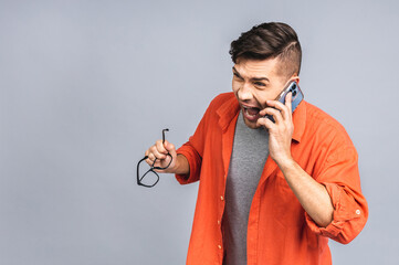 Young caucasian man angry, frustrated and furious with his mobile phone, angry with customer service. Isolated over white grey background.