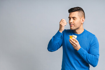 Happy Young ukrainian Handsome Man eating Yogurt isolated over grey white Background. Healthy lifestyle concept.