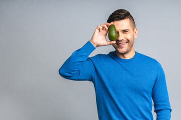 Smiling ukrainian young man holding fresh avocado fruit showing isolated over grey white background...