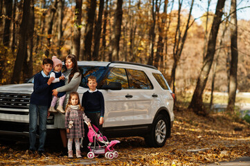 Mother stand near white suv car with four kids in autumn park. Family walk in fall forest.