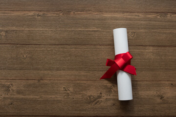 Diploma con moño rojo en mesa de madera © Gabriela