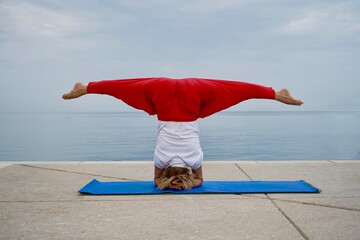 Woman practices balance asanas in yoga session on a beach. Yoga Wide-Legged Headstand Pose, Salamba Sirsasana