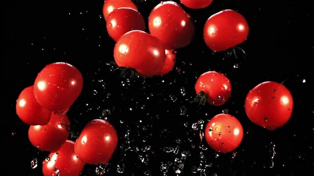 Tomatoes with splashes of water take off and rotate in flight. On a black background. Filmed is slow motion 1000 fps.