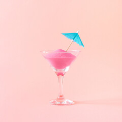 Creative layout made of martini glass, color sand and sun umbrella on a pastel pink background. Party drink concept. Minimal summer idea.