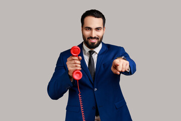 Positive man pointing finger at camera, holding red vintage landline phone, interested in retro...