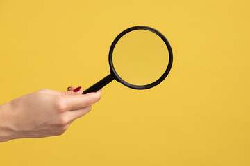 Profile side view closeup of woman hand holding magnify glass, loupe. Indoor studio shot isolated...