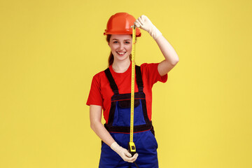 Portrait of woman builder holding roulette for measuring, looking at camera with satisfied facial...