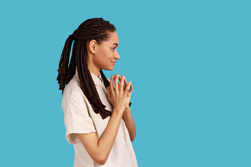 Side view of thoughtful woman with black dreadlocks schemes something, keeps fingers together,...