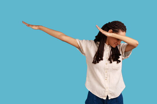 Portrait of happy woman with black dreadlocks showing dab dance, popular internet meme pose, celebrating success victory, dabbing trends concept. Indoor studio shot isolated on blue background.