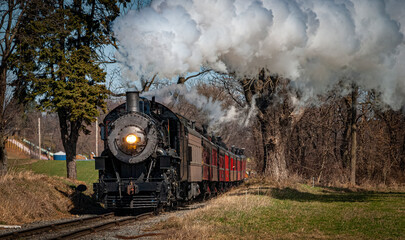 Fototapeta na wymiar An Antique Steam Passenger Train Approaching on a Single Track Blowing Smoke on a Sunny Day