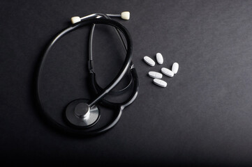 stethoscope and pills lie on a black background with copy space