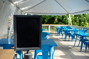 Obraz premium Selective focus on an empty black sign in front of a reserved seating area filled with blue chairs under an outdoor canopy