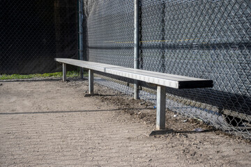 Angled view of a metal bench inside a baseball dugout at a sports field - obrazy, fototapety, plakaty
