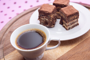 Uma xícara com café e palha italiana sobre madeira, sobre superfície cor-de-rosa. 