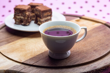 Uma xícara com café e palha italiana sobre madeira, sobre superfície cor-de-rosa. 