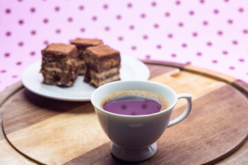 Uma xícara com café e palha italiana sobre madeira, sobre superfície cor-de-rosa. 