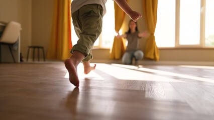 Happy family. Baby feet walk on floor towards mother. Child makes steps barefoot on parquet floor in children room. Son runs to his mother on the laminate with his bare feet. happy baby first steps - Powered by Adobe