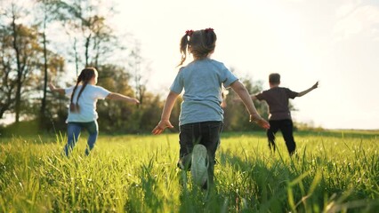 Group of happy children in park on green grass. Spring run outdoors. Cheerful smiles of children running across the lawn. Active family of people in the summer park. Children play and run on grass - Powered by Adobe