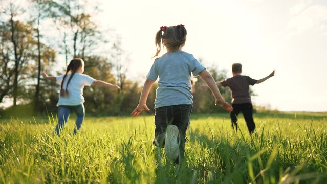 Group of happy children in park on green grass. Spring run outdoors. Cheerful smiles of children running across the lawn. Active family of people in the summer park. Children play and run on grass