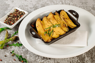 Dish of fried pieces of potatoes with cheese and herbs on grey textured background