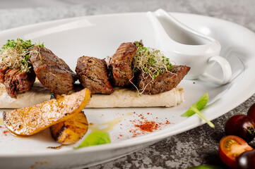 Dish of tasty grilled barbecue meat with potatoe and herbs on grey concrete background