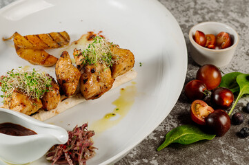 Dish of tasty grilled barbecue meat with potatoe and herbs on grey concrete background