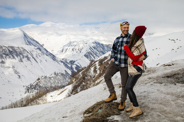 A loving couple plays together in the snow outdoors. Winter holidays in the mountains. Man and woman in knitted clothes have fun on weekends.